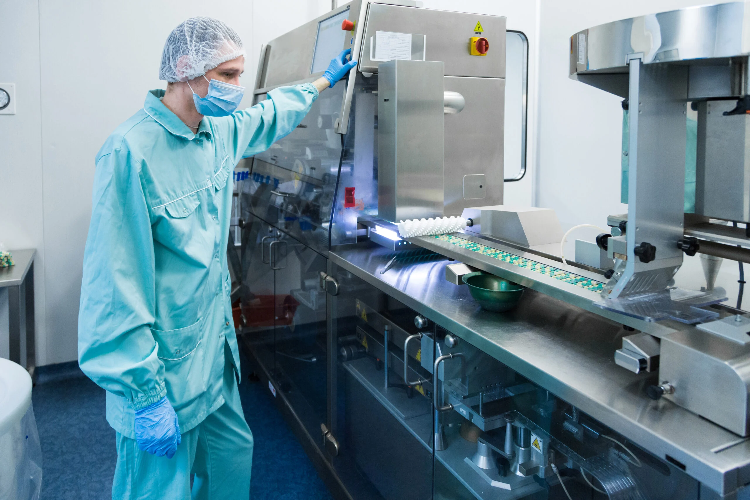 Worker in protective clothing operating pharmaceutical production equipment